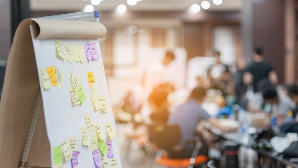 Flipchart mit Workshopteilnehmerinnen und -teilnehmer im Hintergrund